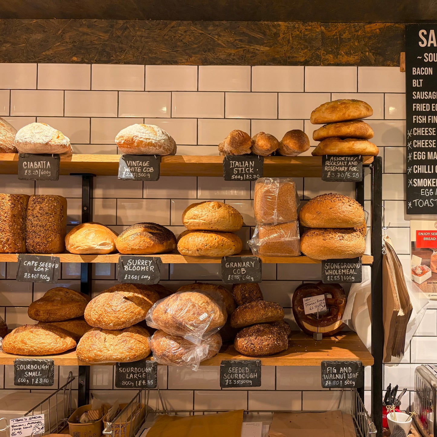 Display of various bread loaves on shelves with a sandwich menu in the background.