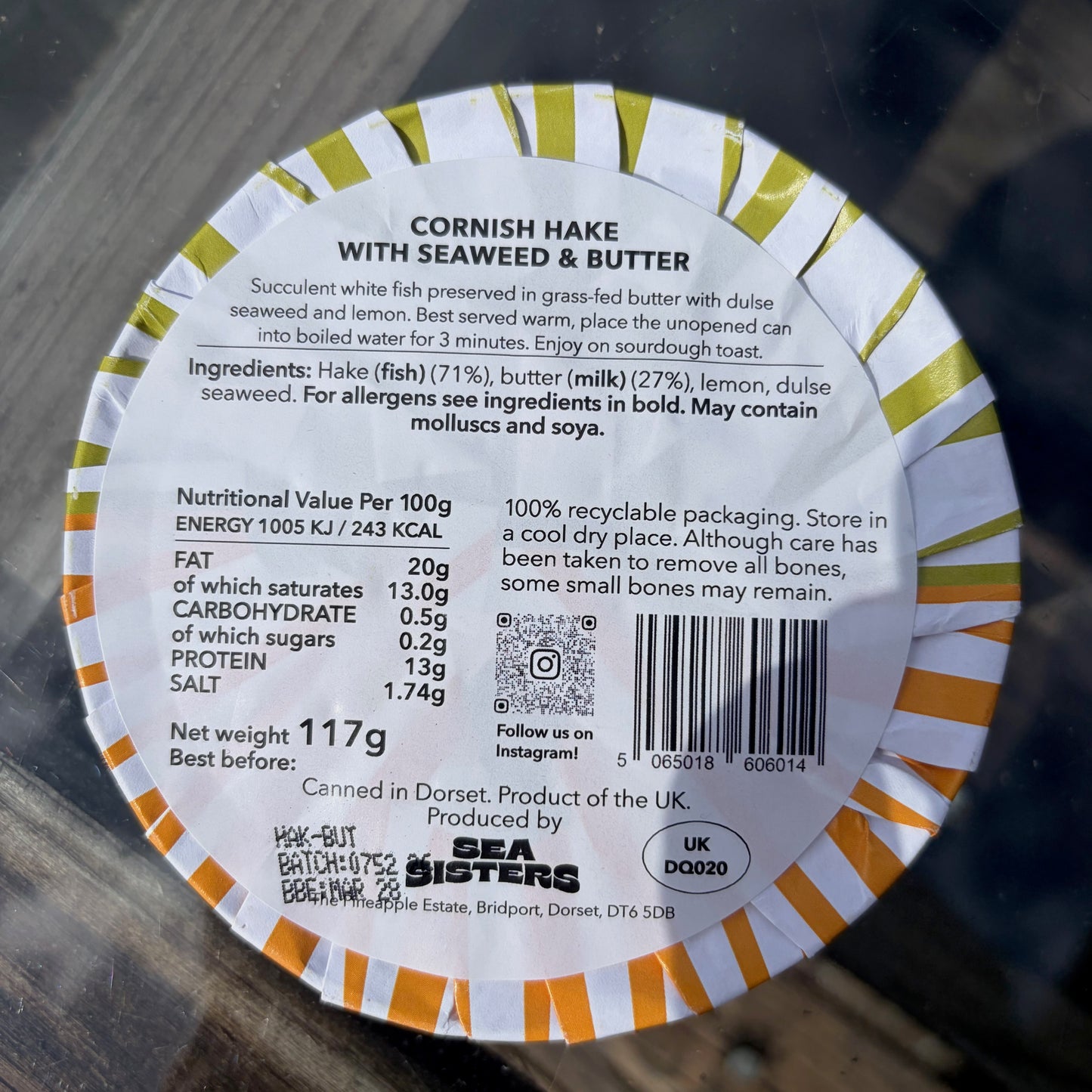 Round label with text and nutritional information for Cornish Hake with Seaweed and Butter on a wooden surface.