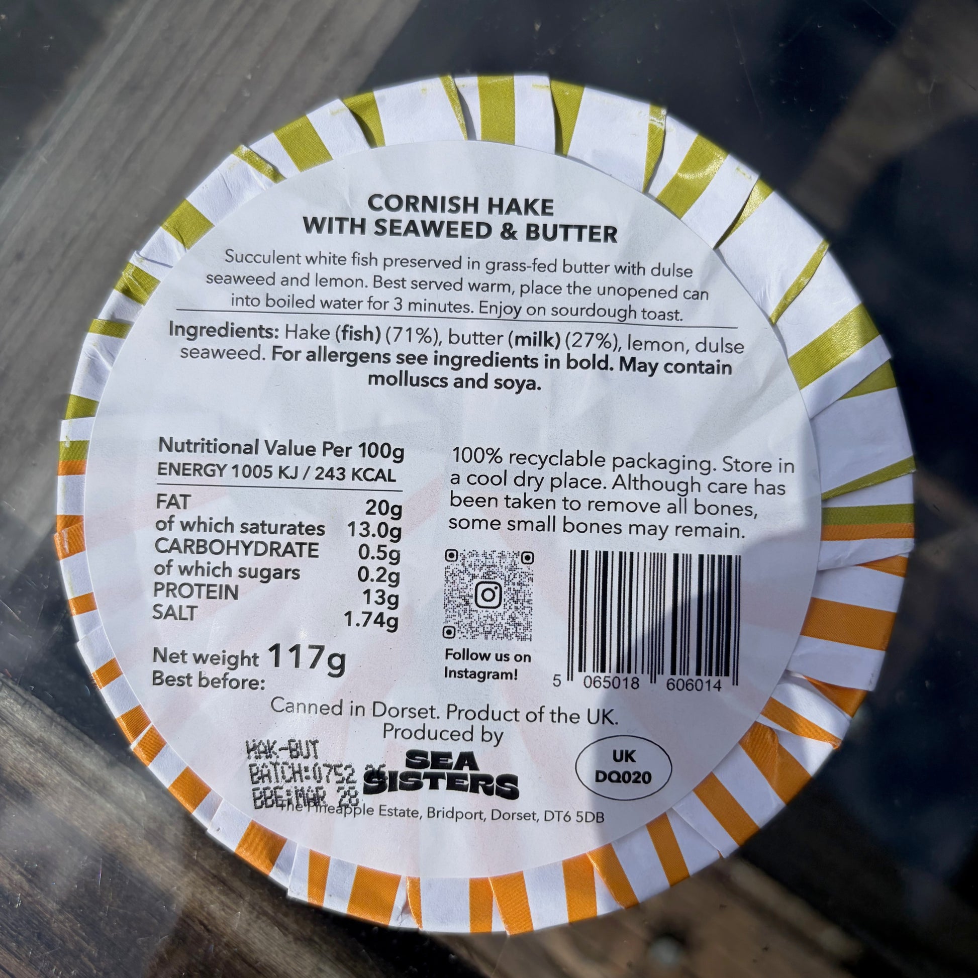 Round label with text and nutritional information for Cornish Hake with Seaweed and Butter on a wooden surface.