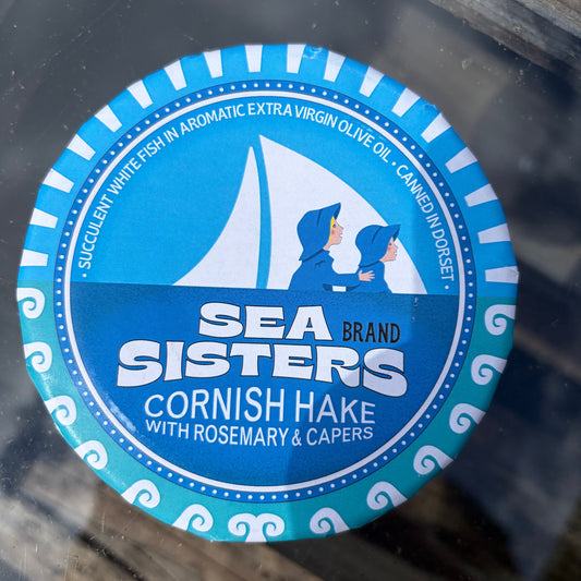 Sea Sisters cornish hake with rosemary and capers tin in blue packaging on glass surface