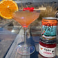 A Mai Tai cocktail in a coupe glass with an orange slice garnish and cherries on a wooden table, next to a can of Whitebox Mai Tai and a jar of Opies Cocktail Cherries.