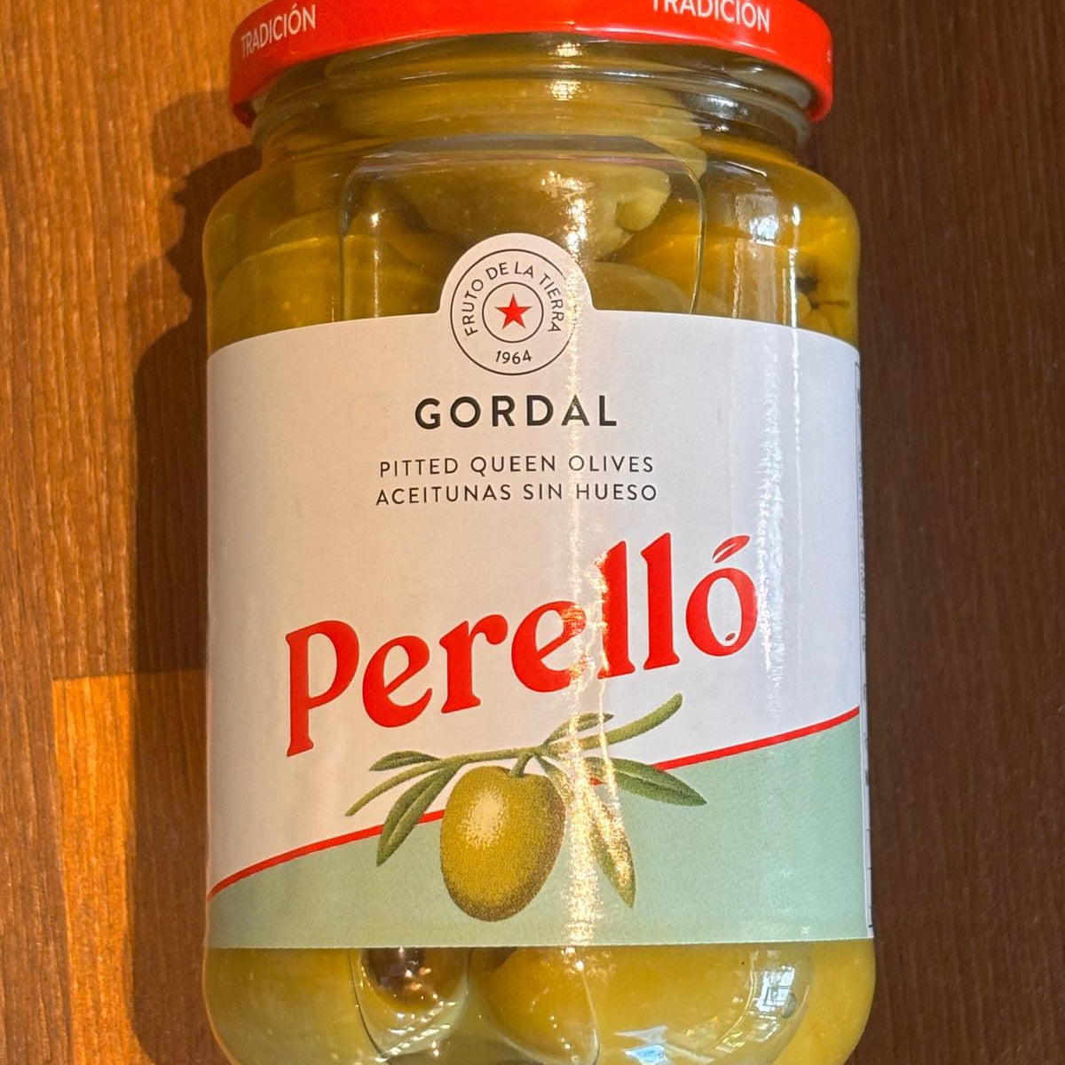 A jar of perello gordal olives on a wooden surface.