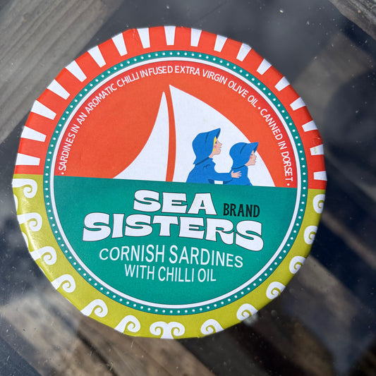 Sea sisters packing, round tin, cornish sardines with chilli oil on a glass table. 