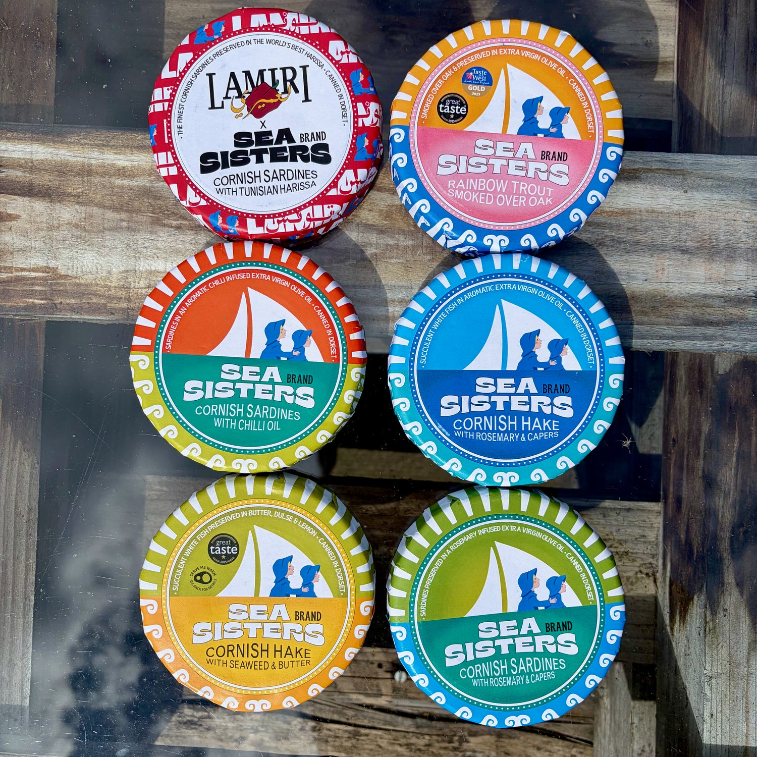 Collection of Sea Sisters brand tins on a glass and wooden surface