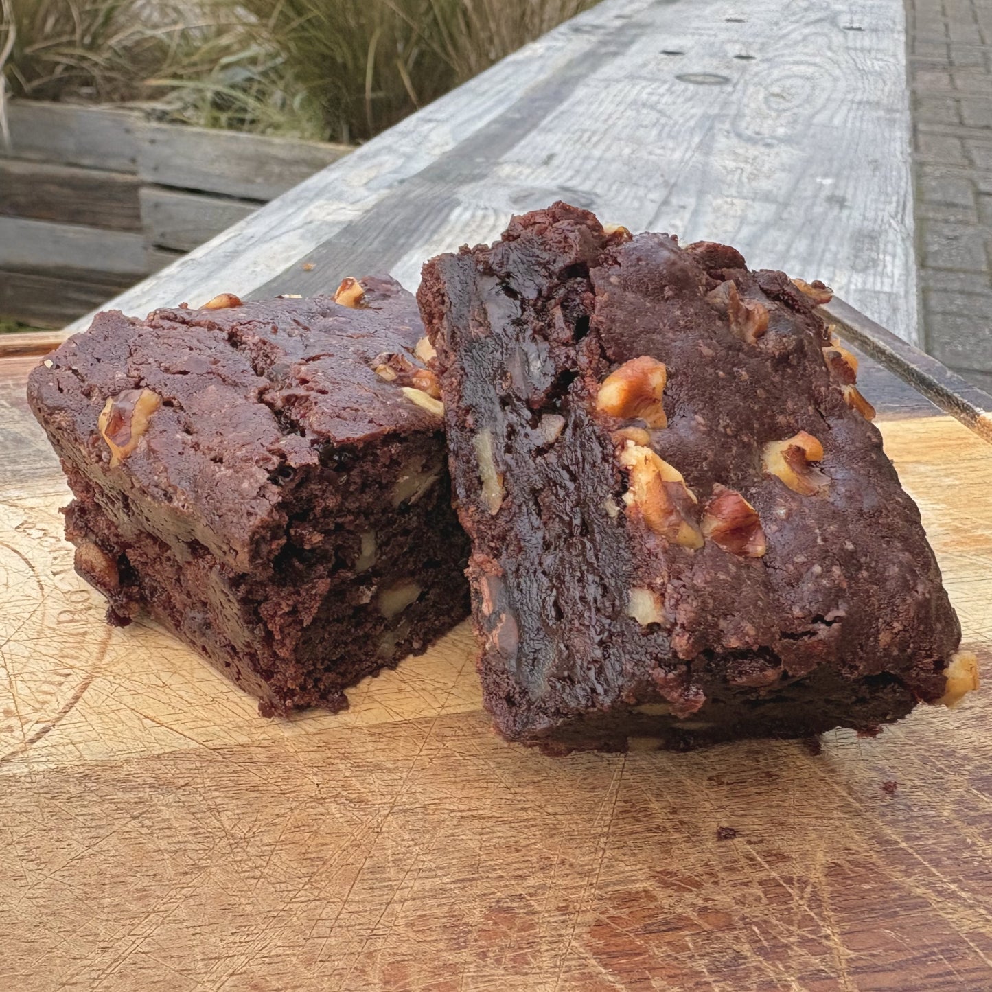 Two vegan walnut chocolate brownies atop a wooden board.