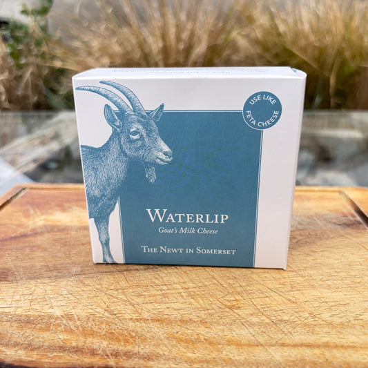 Box of Waterlip goat's milk cheese on a wooden surface with plants in the background