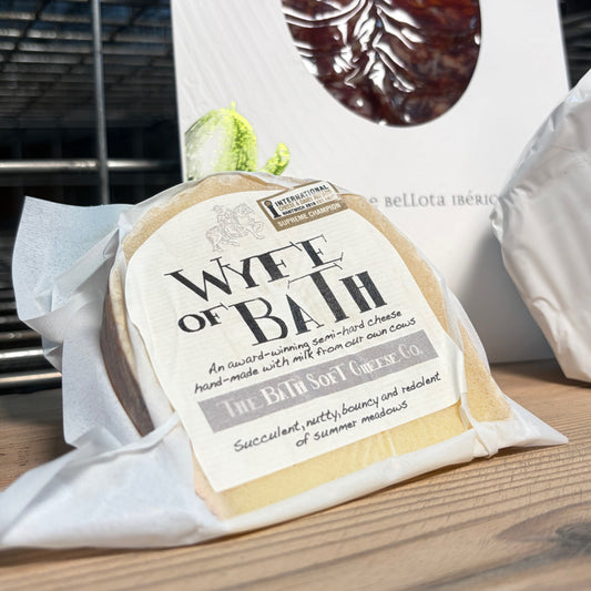 Cheese wedge with 'Wyfe of Bath' label on a wooden surface
