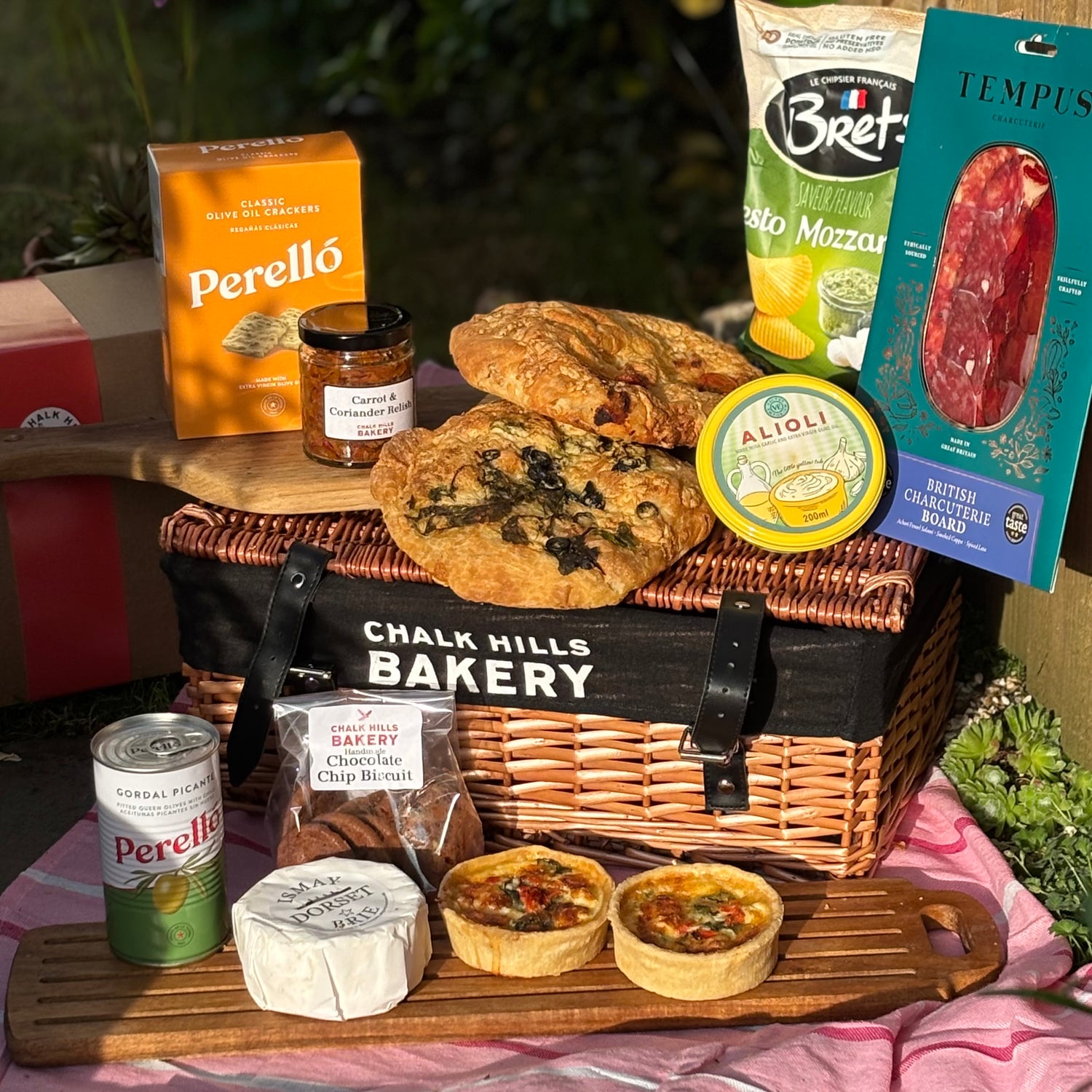 Gourmet food basket with bread, pastries, and packaged items on a table outdoors.